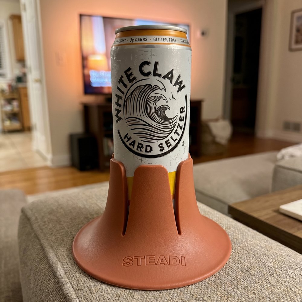 A can standing in a terracotta Steadi on a sofa cushion in a lamp-lit living room.